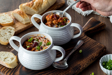 Crocks of chili con carne with crusty bread in behind.