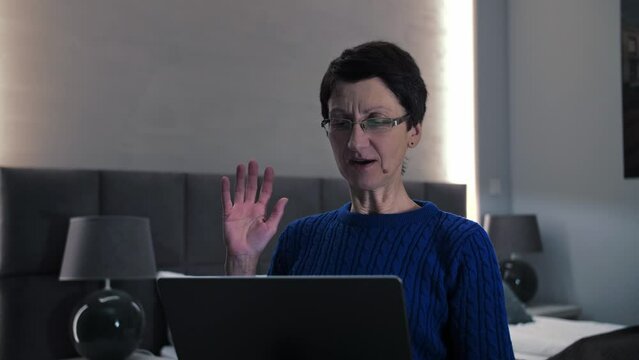 Senior woman make video call waves hand sitting on the couch.Middle age lady using laptop for communication online, webcam zoom conference at home.