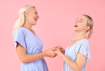 Happy young beautiful woman with her mother holding hands together on pink background