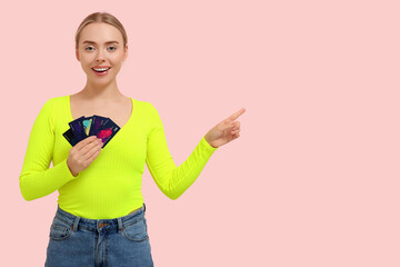 Pretty young woman with credit cards pointing at something on pink background