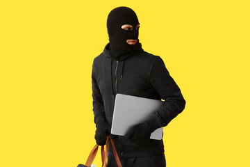 Male thief with laptop on yellow background