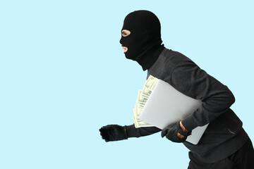 Male thief with laptop and dollar banknotes on blue background