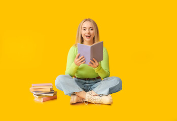 Beautiful young happy woman with many books sitting on yellow background
