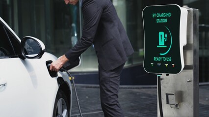Businessman recharge his electric car from charging station at city center or public car park. Eco...