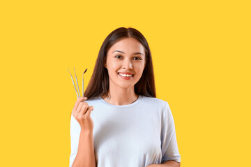 Smiling young Asian woman with dental tools on yellow background