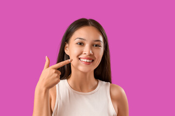 Young Asian woman pointing at her smile on purple background