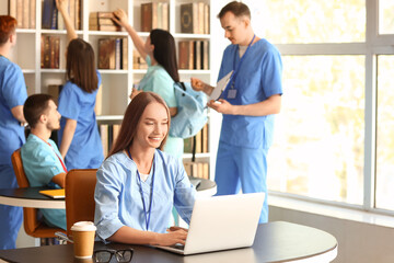 Female medical student studying with laptop in library