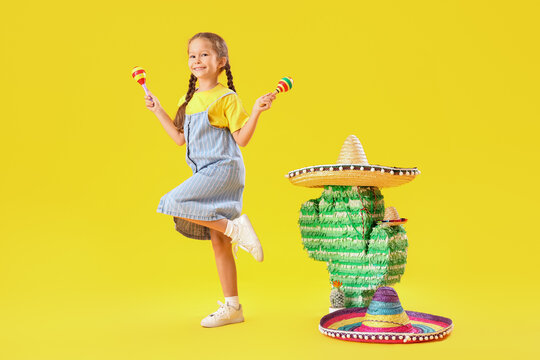 Little girl with maracas, sombrero hats and Mexican pinata on yellow background