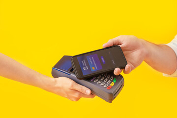 Man with mobile banking paying via terminal on yellow background, closeup