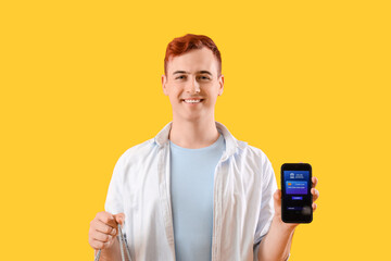 Young man with mobile banking and shopping bag on yellow background