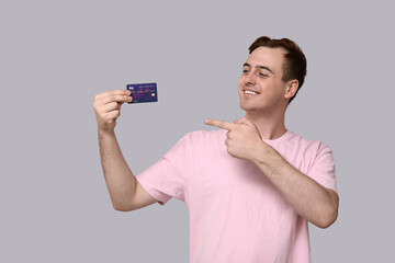 Young man pointing at credit card on grey background