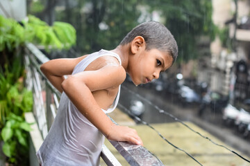 Little kid playing in summer rain in house balcony, Indian smart boy playing with rain drops during monsoon rainy season, kid playing in rain