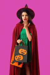 Surprised young woman dressed for Halloween as witch with gift bags on purple background