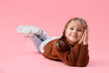 Cute little girl in warm sweater lying on pink background