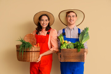 Young farmers with fresh vegetables on beige background