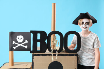 Little boy dressed for Halloween as pirate with cardboard ship on blue background