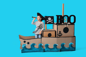 Little girl dressed for Halloween as pirate with cardboard ship on blue background