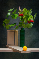 A branch of red viburnum in a green vase with orange ball