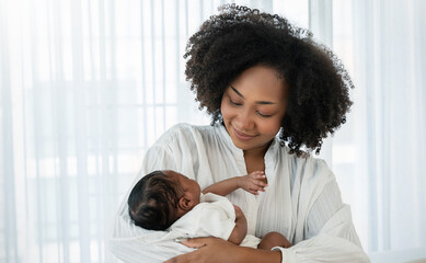 Close up portrait of beautiful young African American  mother holding sleep newborn baby in...