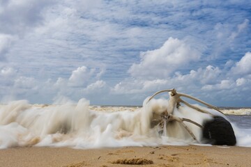 Sea wave crashing against old wood on beach with clouds as background