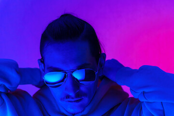 Portrait of a young man in profile at studio. Male model in colorful bright neon lights posing on purple background