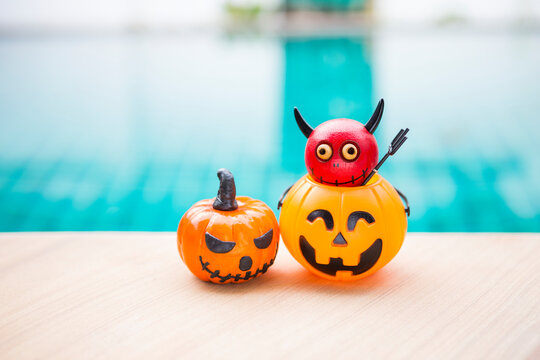 Red devil in Halloween pumpkin lantern on swimming pool edge, outdoor day light, Halloween decoration item