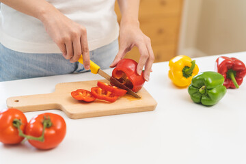 Cooking healthy diet food with capsicum, hand of housewife asian young woman cutting red bell pepper cutting on wood board by knife in kitchen at home, fresh vegetable from nature organic for wellness