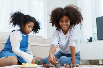 Happy lovely cute American - African black ethnicity girl and mother enjoy playing a plastic dinosaur toys together.