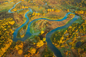Aerial view of landscape of a winding river in autumn morning. The sky is reflected from the surface of the river. Sunbeams illuminate the trees and grass and change their color to light green.