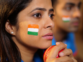 Bokeh shot of a female with a face painted in three colors of Tiranga - holding a cricket ball in...