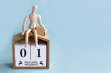 New Year concept. One day before the holidays of the year. Wooden man sitting on a house on a blue background