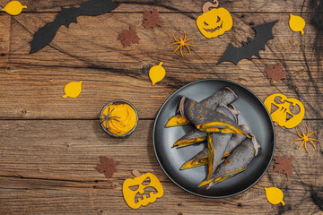 Halloween sweet dessert with traditional decor. Thin black pancakes with pumpkin cream, fall leaves
