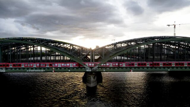 Drone flight over an old bridge on the river Elbe in Hamburg. A train passes over the bridge and the sun slowly sets over the city.