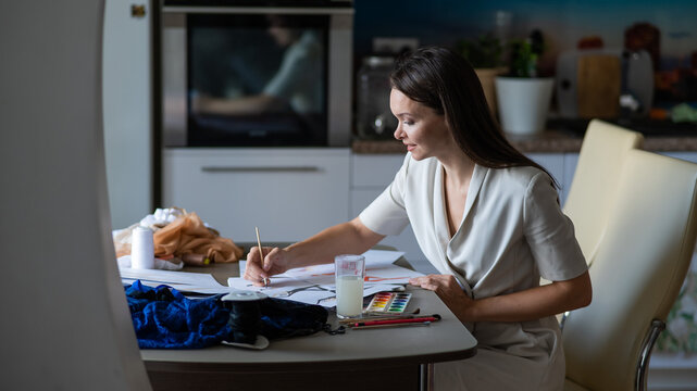 Woman drawing sketches of swimwear and underwear in watercolor while sitting in the kitchen. 