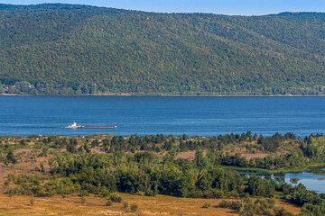 A tug pulls a barge along the Volga River near the city of Samara, Russia. Blue water, sandy shore,...