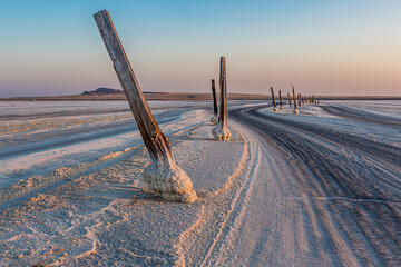 Road on salt lake Baskunchak (Russia), marked with logs at sunset or sunrise. The base of the logs...