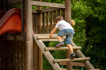 Little boy climbing on a wooden ladder in a children's playground.