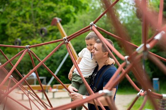 Father And Son Having Fun On A Climbing Net In The Park.