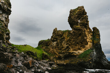 People hike on green hill with rock formations on the coast