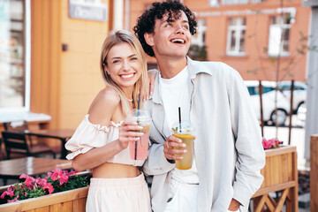 Young smiling beautiful woman and her handsome boyfriend in casual summer clothes. Happy cheerful family. Female having fun. Couple posing in street. Holding and drinking cocktail drink in plastic cup