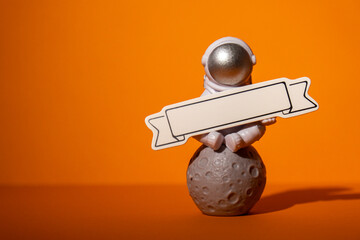Plastic toy astronaut with paper note template mock up for your text on colorful orange background...