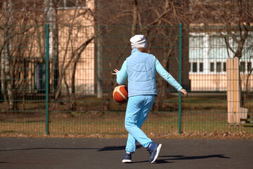 A child of 10 years old plays basketball on an open sports ground. Girl playing with a ball outdoors on an autumn day.