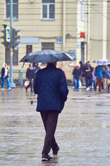 An adult man walks down the street under a black umbrella. It's raining, autumn cloudy day in the city.
