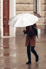 A young girl hurries to the store under a white umbrella. Rainy weather on an autumn day outside.