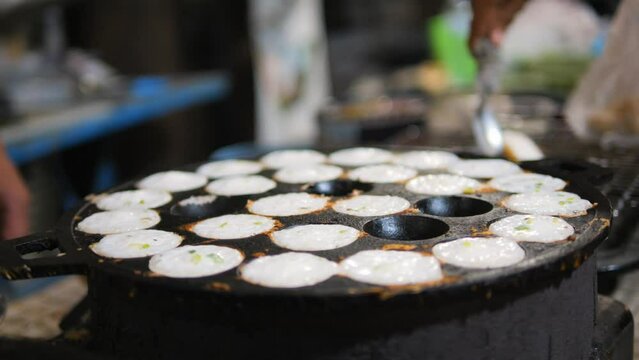 Asian street food: traditional Thai Kanom Krok dessert coconut-rice pancake cooked in a special pan with half-spherical molds, high quality 4K slowmotion hedonism travel concept footage, Thailand.