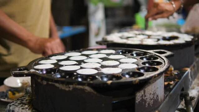 Asian street food: traditional Thai Kanom Krok dessert coconut-rice pancake cooked in a special pan with half-spherical molds, high quality 4K slowmotion hedonism travel concept footage, Thailand.