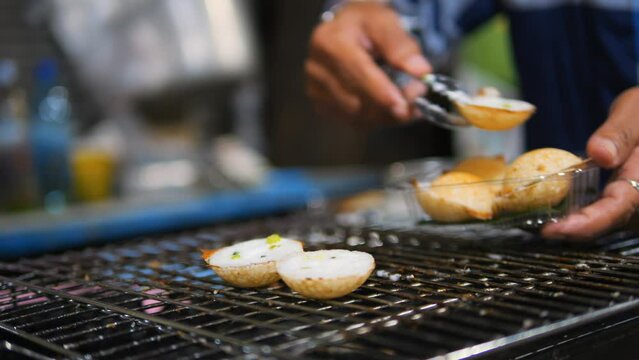 Asian street food: traditional Thai Kanom Krok dessert coconut-rice pancake cooked in a special pan with half-spherical molds, high quality 4K slowmotion hedonism travel concept footage, Thailand.