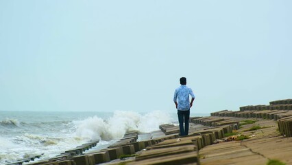 Lone Man Lighting Cigarette While Walking Over The Coast With Block Stone Breakwater. Static Shot