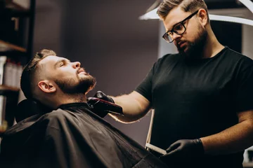 Tuinposter Handsome man cutting beard at a barber shop salon © Petro