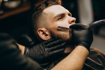 Handsome man cutting beard at a barber shop salon